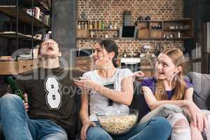 Happy young friends sitting on sofa and eating popcorn from glass bowl
