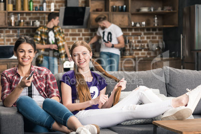 Young smiling women sitting on sofa and watching tv at home