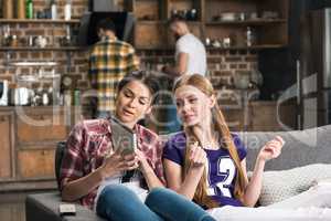 Two young women discussing cd box while sitting on sofa at home