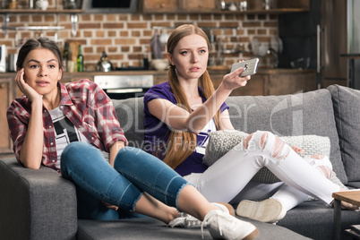 Two emotional young women sitting on sofa and watching tv