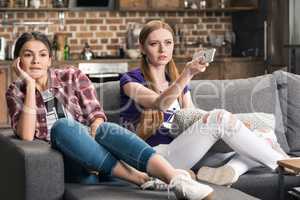 Two emotional young women sitting on sofa and watching tv