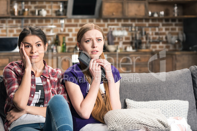 Young scared women sitting on sofa and watching tv