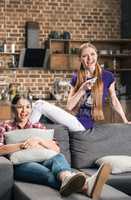 Two laughing young women watching tv with remote control at home