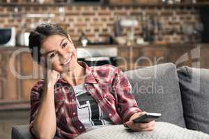 Young smiling woman holding remote control and watching tv at home
