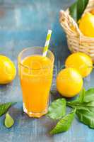 Lemon juice in glass and fresh fruits with leaves on wooden background, vitamin drink or cocktail