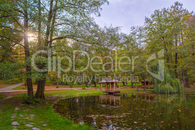 Autumn park with pond and wooden alcoves.