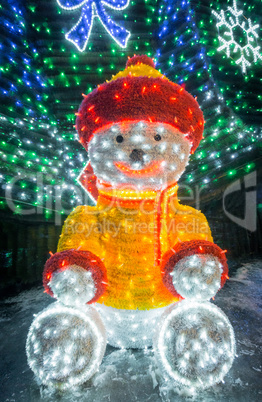 Teddy bear with bright lights and decorated fir.