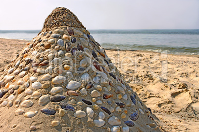 Sandy pyramid with shells on a sea beach