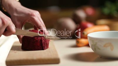 Woman's hands slicing beet on wooden cutting board