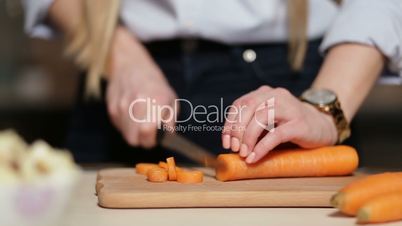 Woman's hand cutting carrot on board with knife