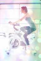 Composite image of woman energetically riding exercise bike