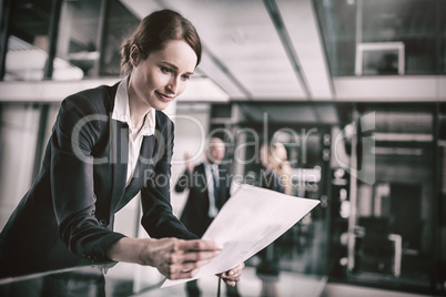 Businesswoman standing in corridor reading document in office Businesswoman standing in corridor reading document in office
