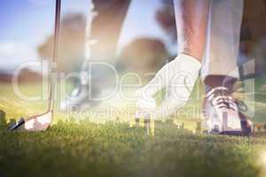 Composite image of golfer placing golf ball on tee