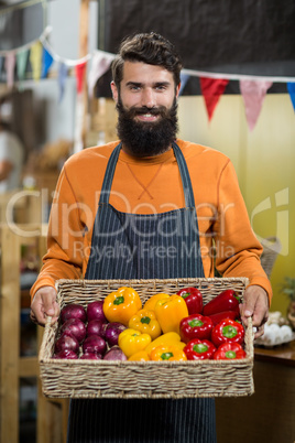 Vendor holding a basket of onion and capsicum at the grocery store