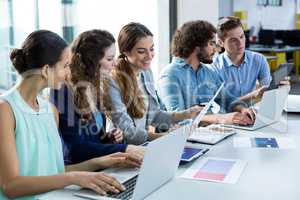 Smiling business team working on laptop and digital tablet in meeting