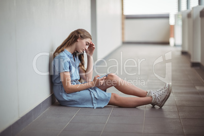 Sad schoolgirl using mobile phone in corridor