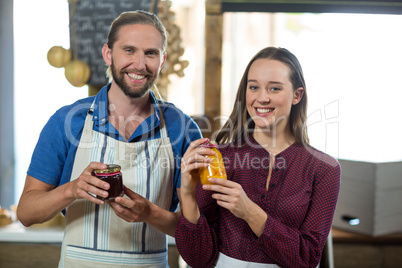 Shop assistants interacting while holding jam and pickle jar at grocery shop