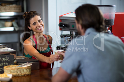 Smiling female staff serving cup of coffee to a customer at counter in shop
