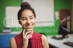 Portrait of smiling schoolgirl standing with hand on chin in classroom