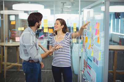 Male and female business executives discussing over whiteboard