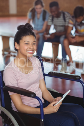 Portrait of disabled schoolgirl using digital tablet with classmates in background