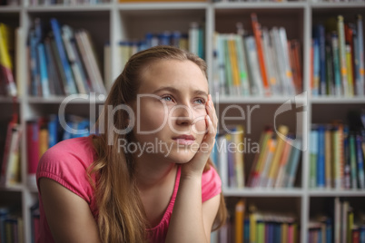 Thoughtful schoolgirl sitting in library