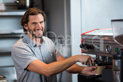 Portrait of smiling male staff making cup of coffee at counter