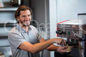 Portrait of smiling male staff making cup of coffee at counter