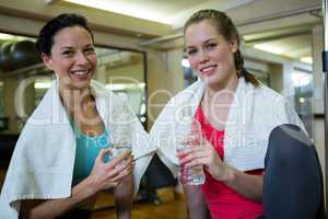 Portrait of happy women holding water bottle while relaxing after workout