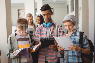 Students standing with notebook and digital tablet in corridor