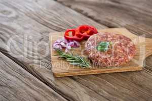 Beef patty and ingredients on wooden tray against wooden background