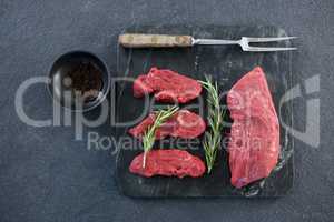 Beef steaks, black pepper and fork on slate plate
