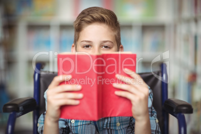 Portrait of disabled schoolboy holding book in library