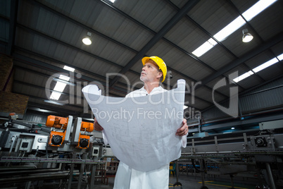 Thoughtful factory engineer holding blueprint
