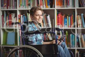 Portrait od disabled schoolboy holding digital tablet in library