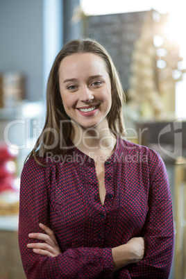 Portrait of smiling female staff standing with arms crossed against counter