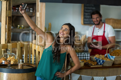 Smiling woman talking selfie with mobile phone at counter