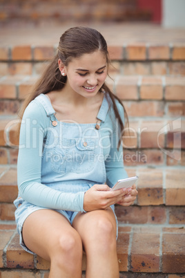 Happy schoolgirl using mobile phone on staircase