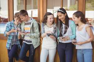 Group of smiling school friends using mobile phone in corridor