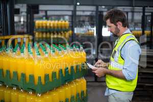 Factory worker maintaining record on juice bottles on digital tablet