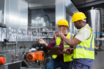 Two factory workers discussing while monitoring drinks production line