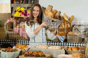 Smiling female staff holding a basket of baguettes at counter