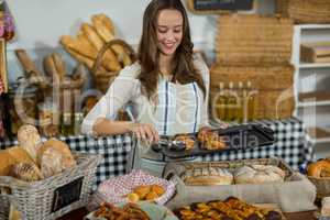 Smiling female staff placing croissant on tray at counter