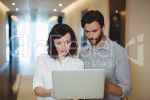 Male and female executives using laptop in corridor