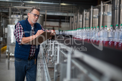 Male factory worker maintaining record on clipboard