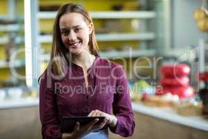 Portrait of smiling female staff using digital tablet at counter