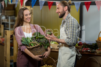 Woman interacting with vendor while holding basket of green leafy vegetables