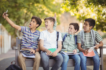 Happy students sitting on bench and taking selfie on mobile phone