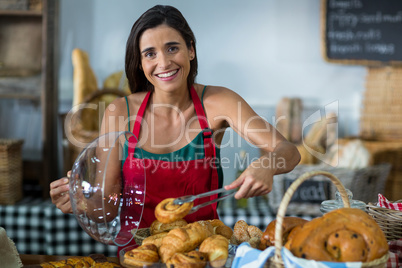 Portrait of smiling female staff holding croissant with tong at counter