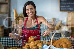Portrait of smiling female staff holding croissant with tong at counter